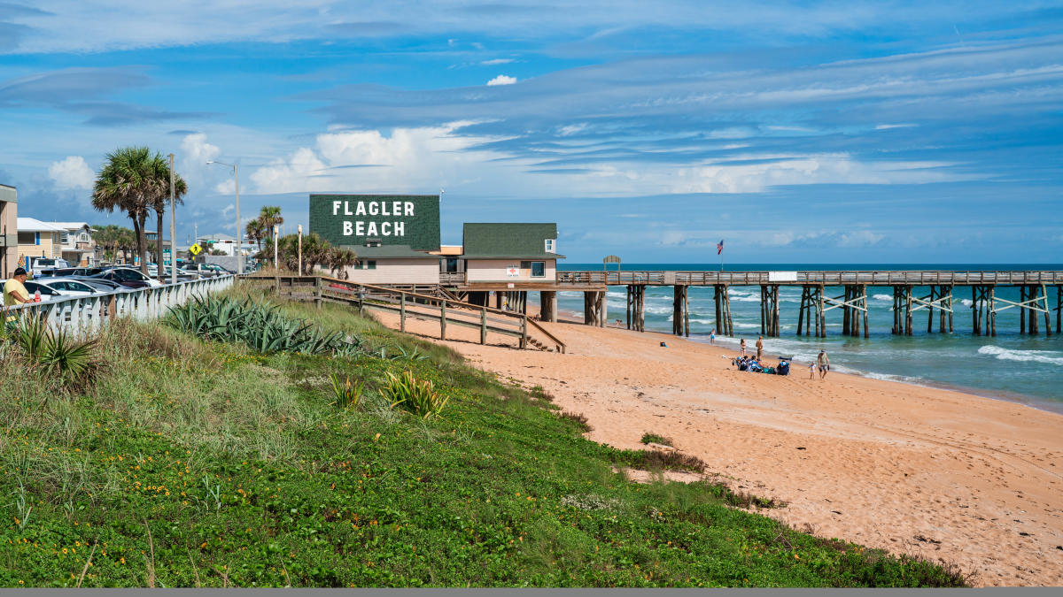 Flagler Beach sign, wooden pier and sandy Atlantic shoreline